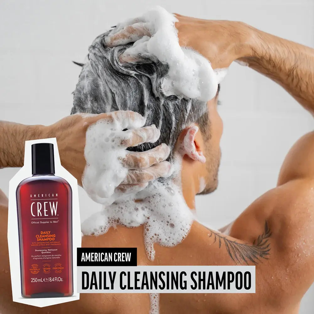 Person washing hair with American Crew Daily Cleansing Shampoo, product displayed on the left.