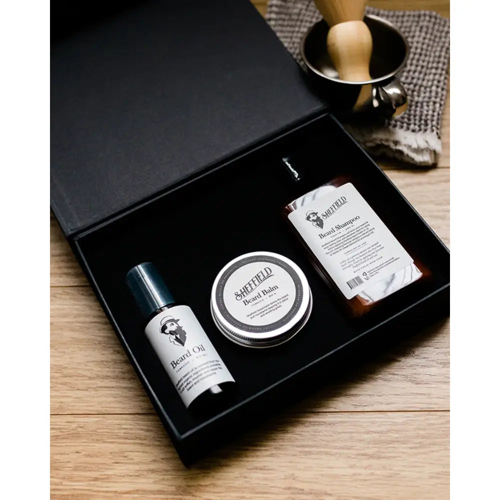 Sheffield grooming products including a bottle, jar, and brush in a black box on a wooden surface.