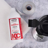 Keratin Colour KC hair color product with a brush and scale on a gray surface